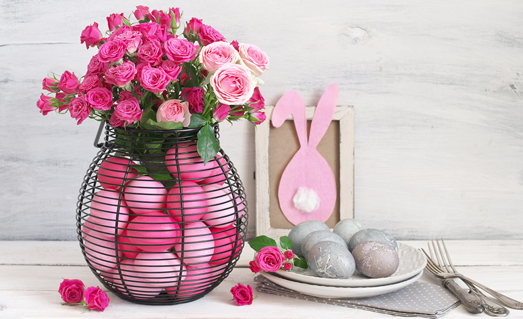 A black wire vase with hot pink faux eggs and roses.