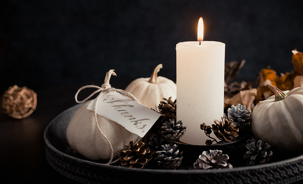 A candle with white pumpkins and candle on a tray.
