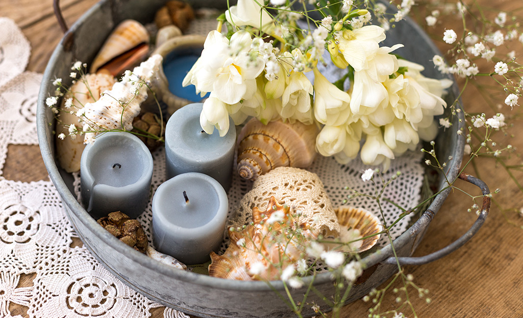 A metal tray with flowers, candles and seashells.