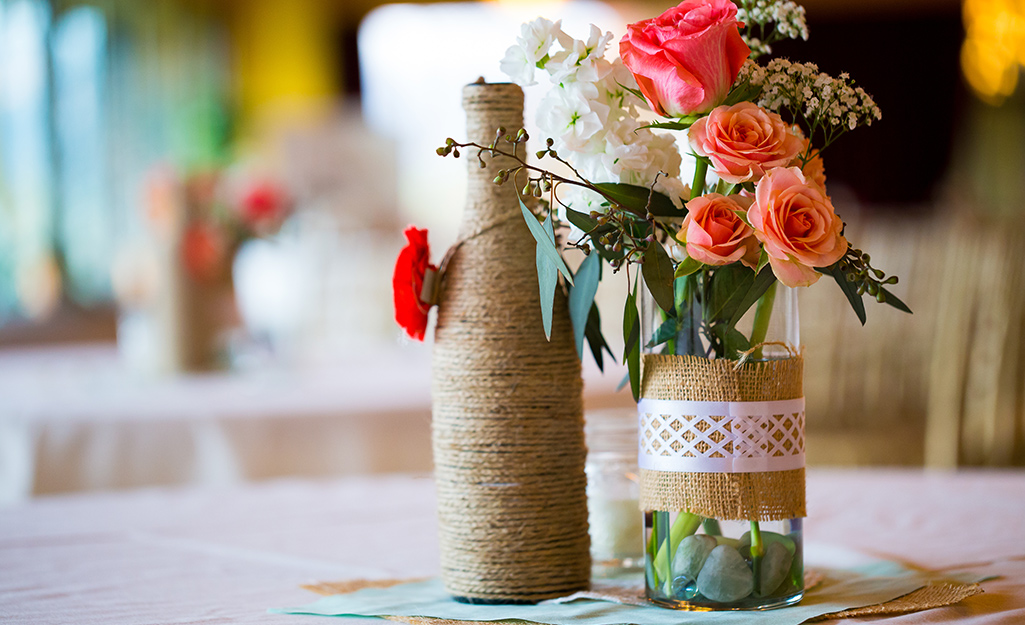 Wine bottle vases wrapped in rope and burlap on a table.