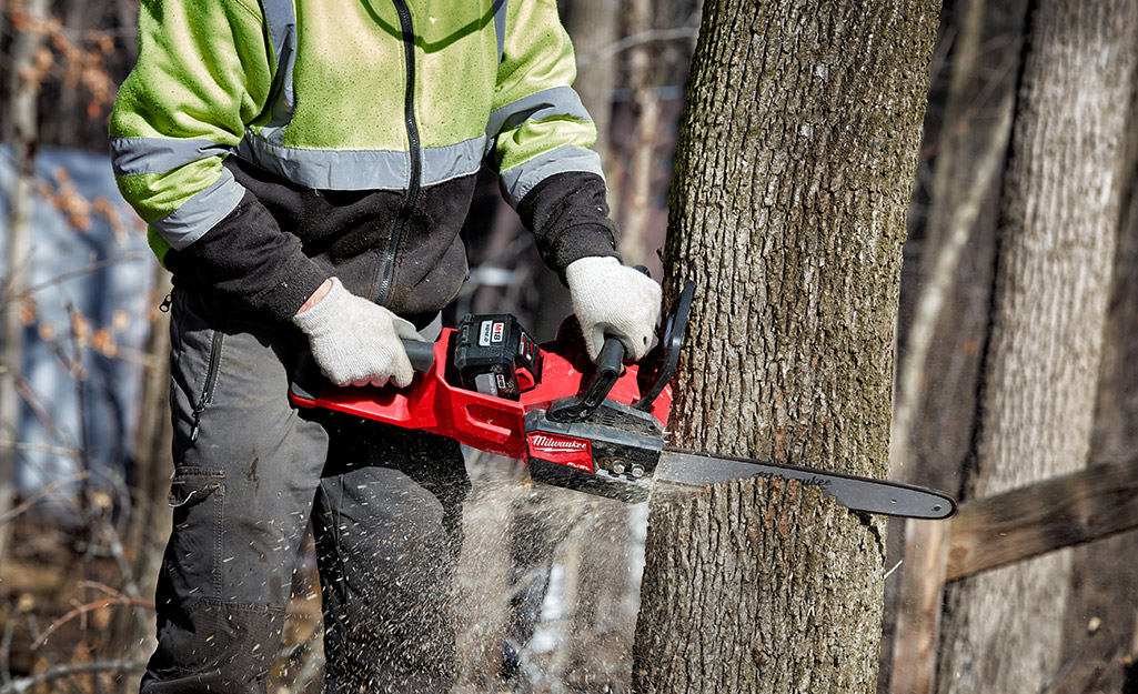 A person with protective gear using a chainsaw to cut a log.