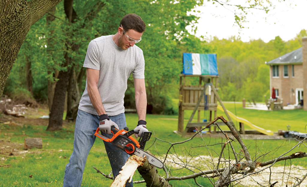 A person using a chainsaw to cut a downed tree limb.