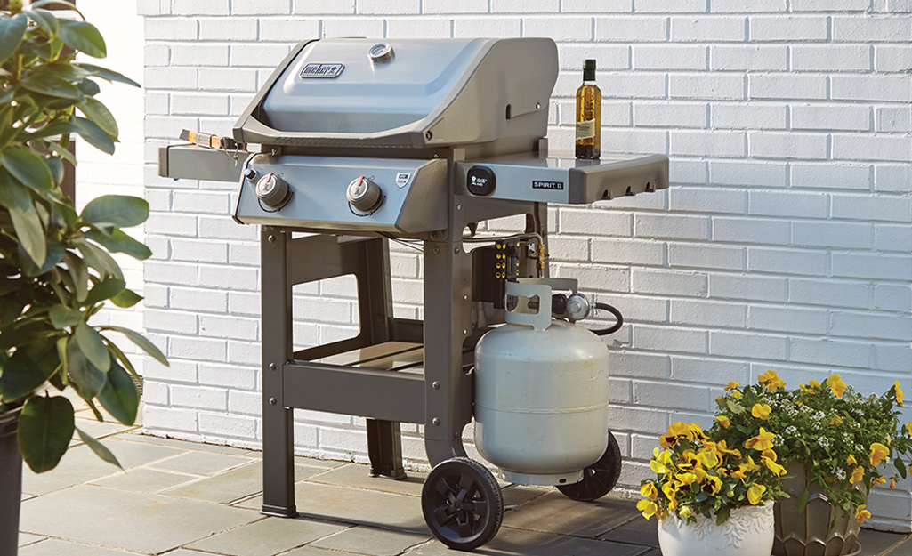 A gas grill with a propane tank on a patio.