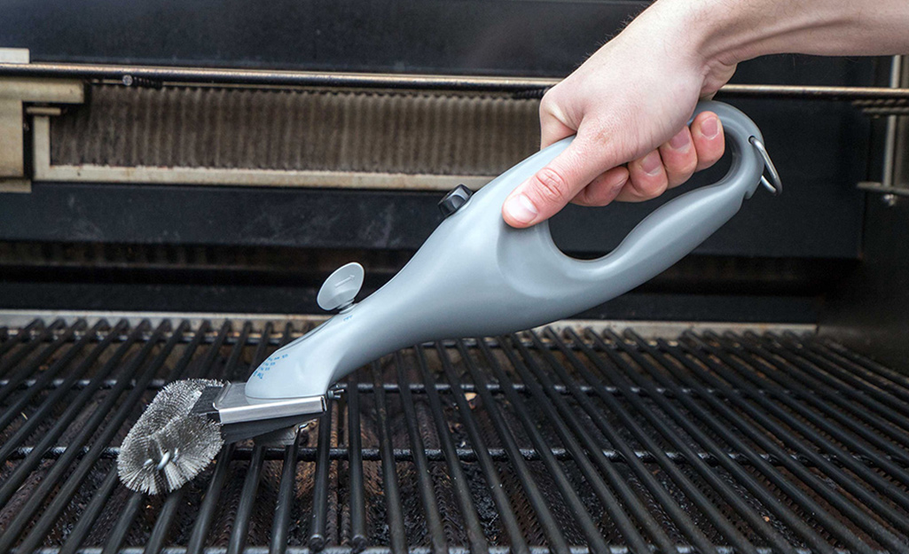 A person using a scrub brush to clean the grates on a grill.