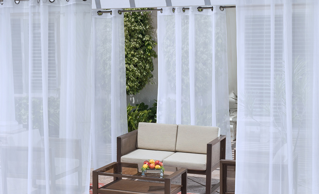 Sheer outdoor curtains surround an outdoor seat.