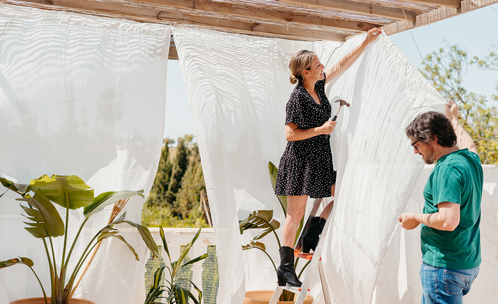Two people hang sheer outdoor curtains.