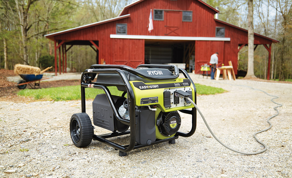 A portable generator on wheels sitting outside a red barn.