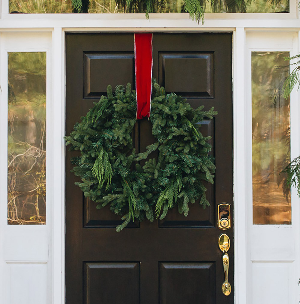 A wreath hanging with red ribbon on a black front door.