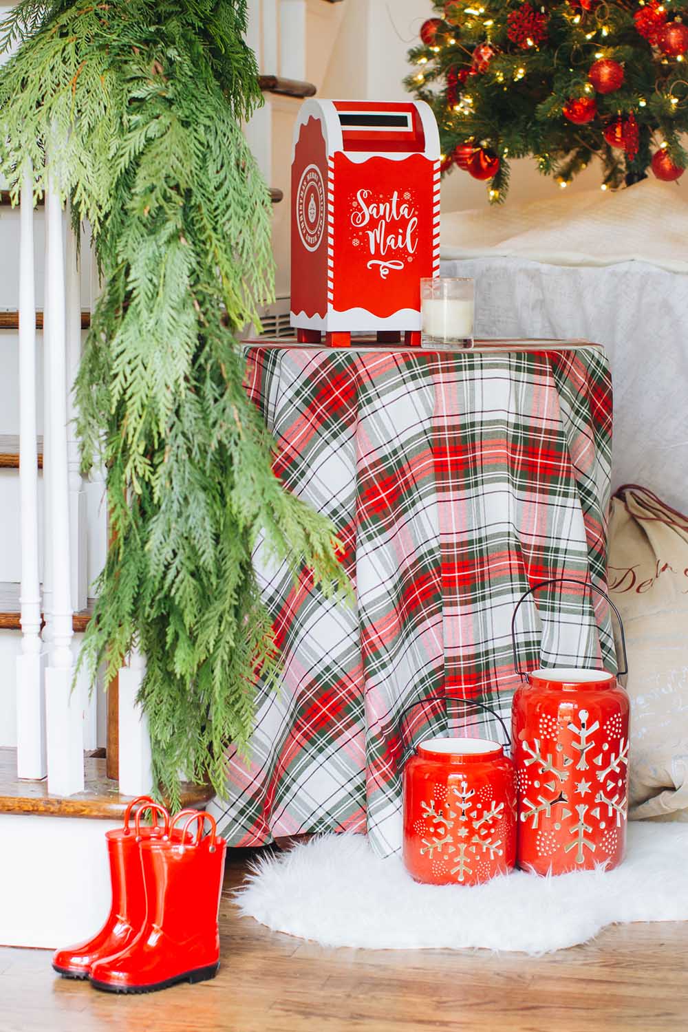 A red Santa mailbox sitting on top of a table decorated with a red and green plaid tablecloth.