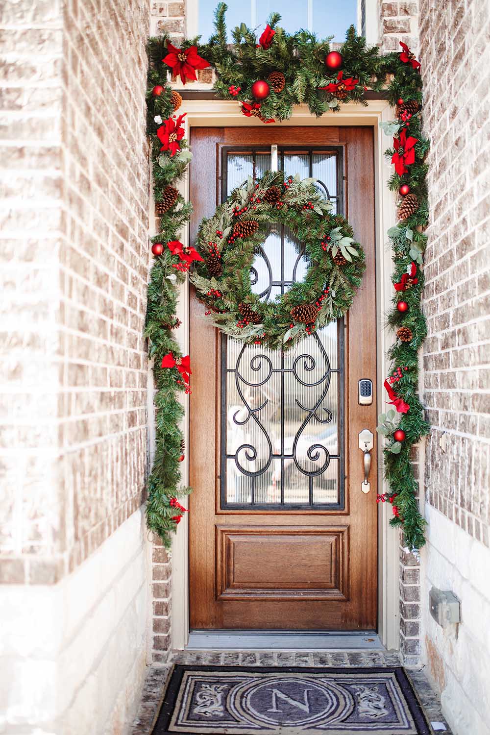 A monogrammed doormat sitting in front of a holiday decorated front door.