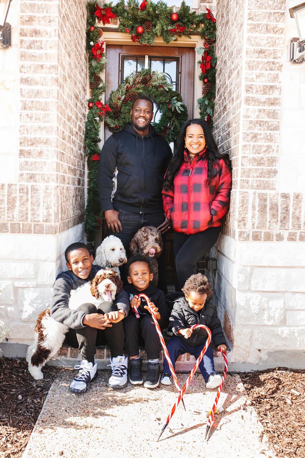 A man, woman, three children, and three dogs pose in front of a holiday decorated front door.