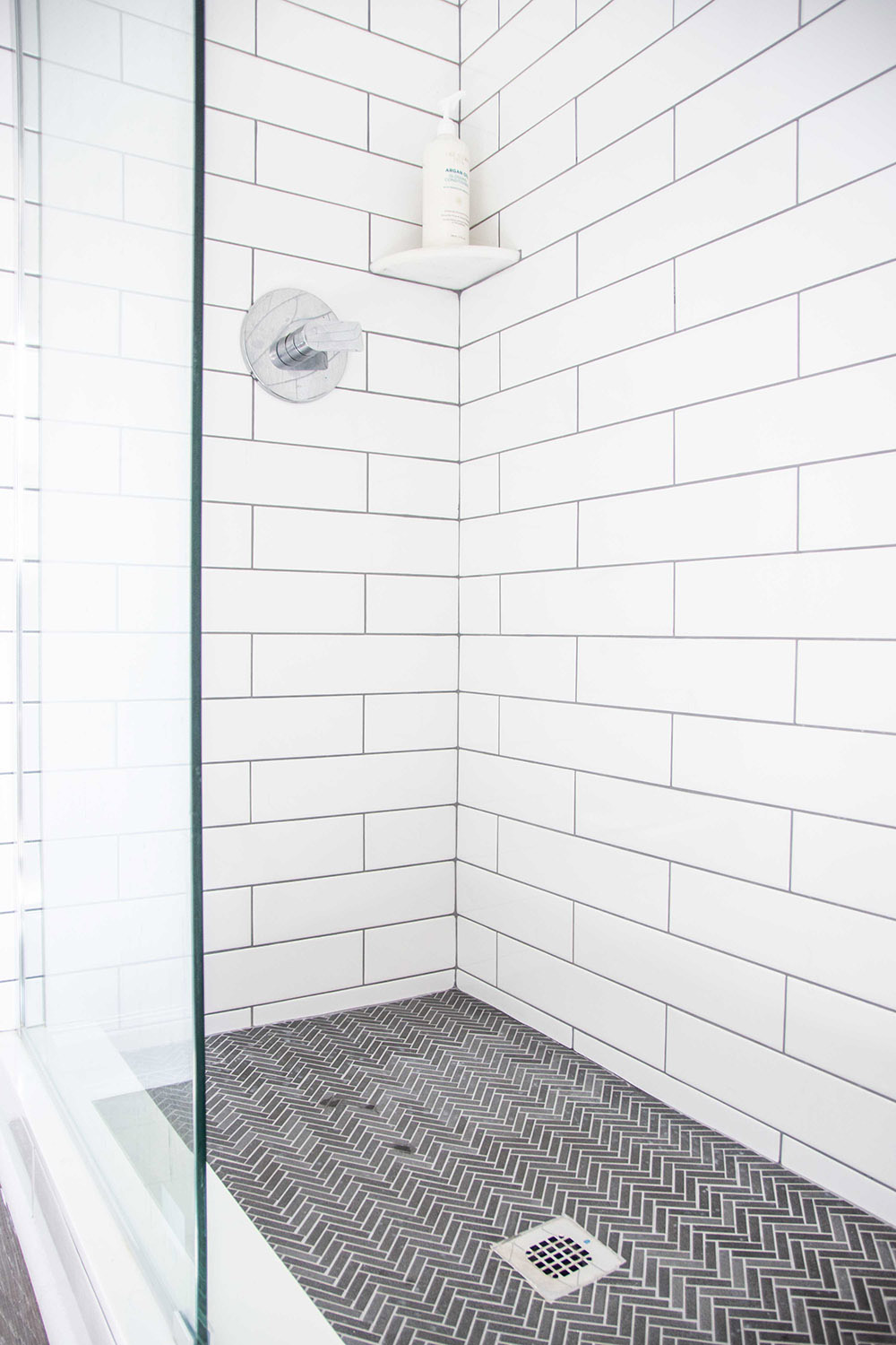 A white tiled shower with chrome hardware.