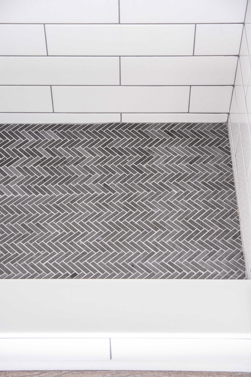 A shower floor with dark mosaic herringbone tile.