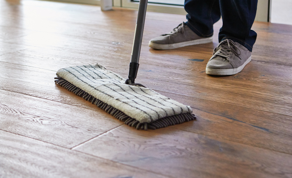 A person wearing gray shoes pushes a flat mop to clean laminate floors. 