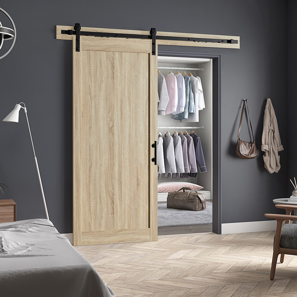 Clothes hang from two rods inside a closet with a barn door in a bedroom with gray walls.