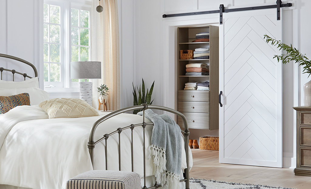 A white barn door opens in front of a closet in a bedroom with an iron bed.