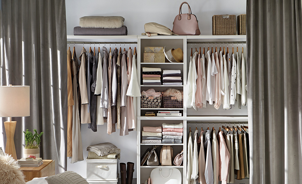 Curtains used instead of a closet door are open to show clothes hanging from rods and folded on shelves.