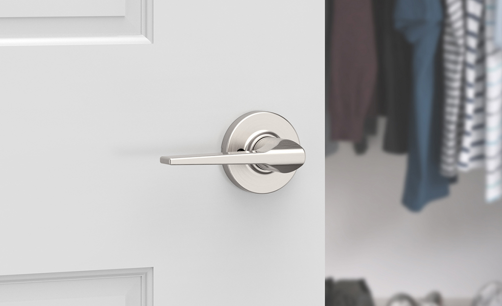A closet door with a silver handle stands open to show clothes inside.