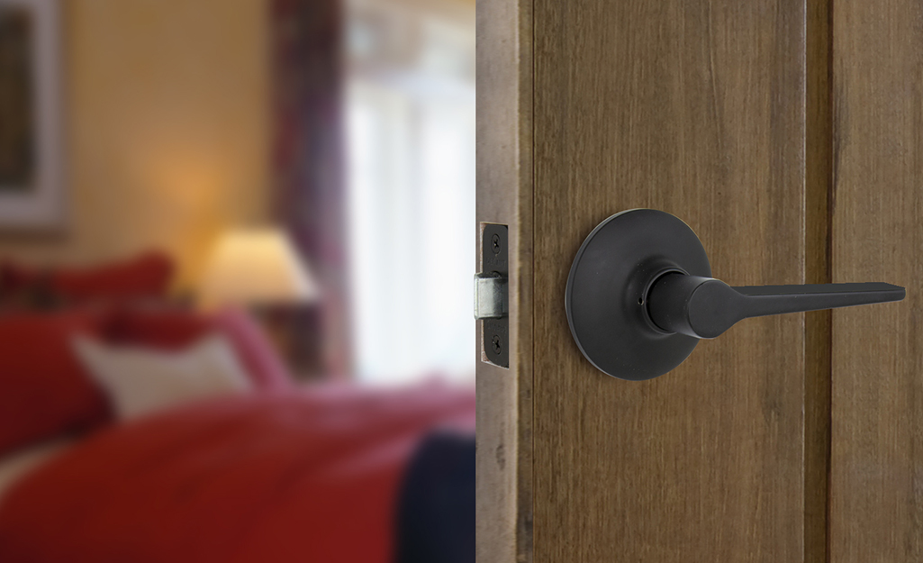 The handle on an open door is shown with a bedroom in the background. The handle on an open door is shown with a bedroom in the background.