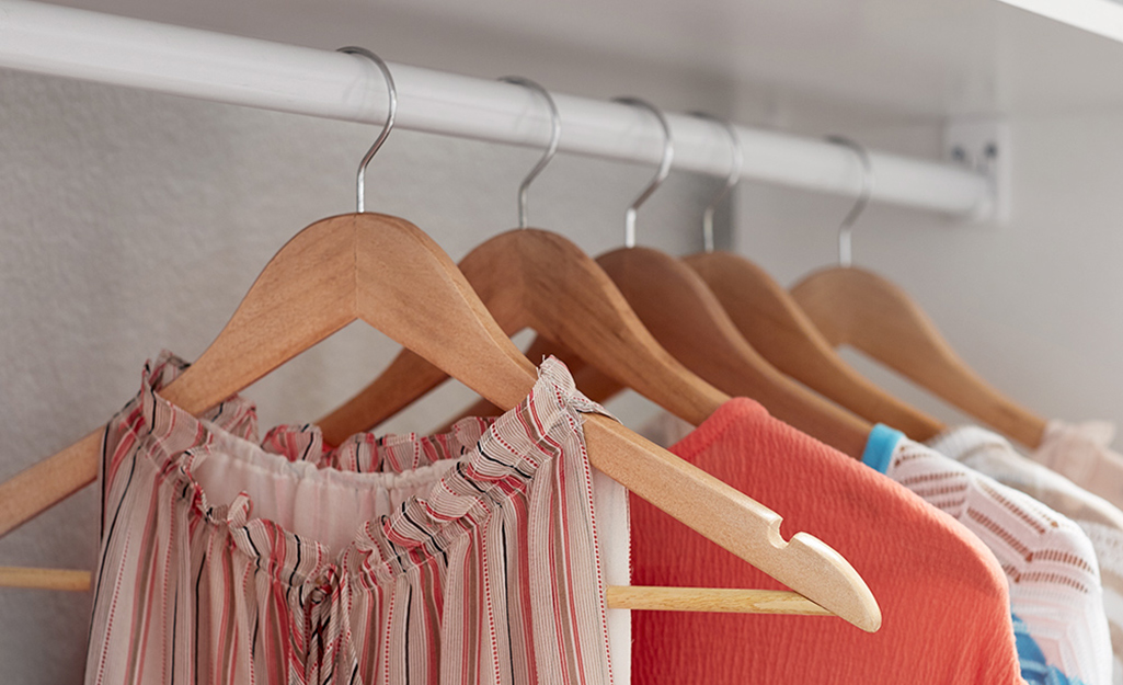 Clothes hang on wood hangers in a closet.