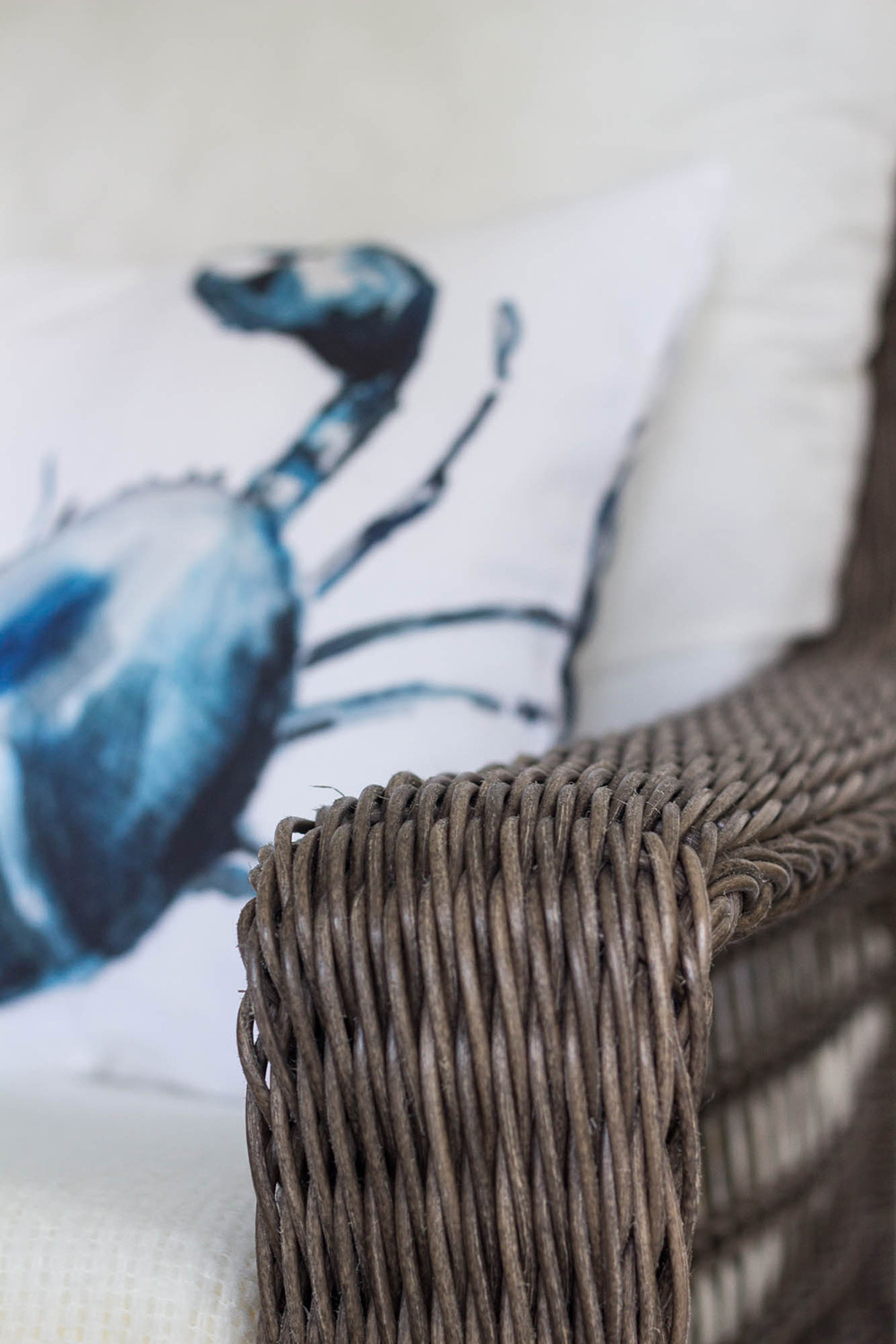 A wicker chair with neutral cushions and a pillow with a blue crab. A wicker chair with neutral cushions and a pillow with a blue crab.