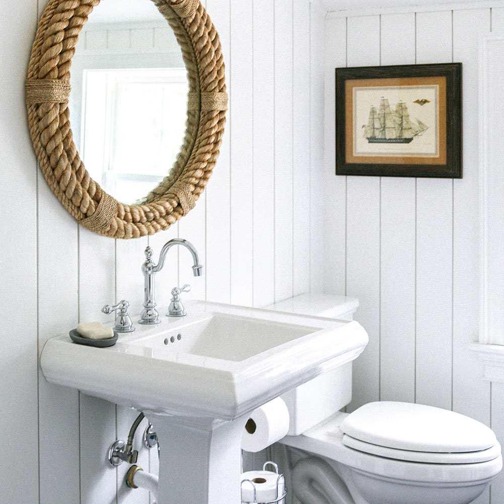 A bathroom with white vertical shiplap walls and a braided rope mirror.