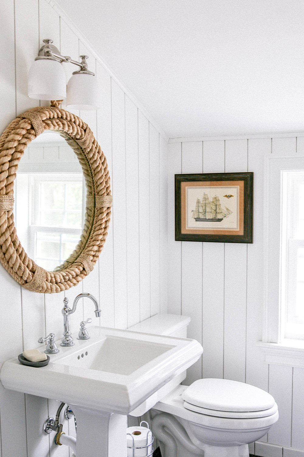 A renovated bathroom with a pedestal sink and white vertical shiplap walls.