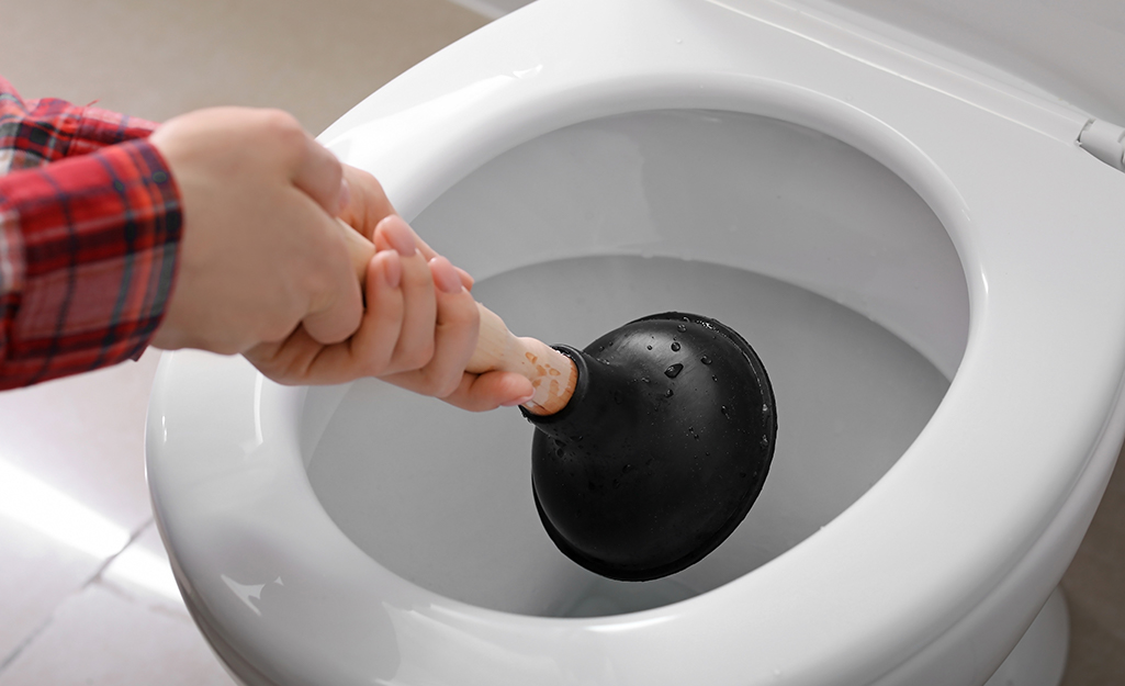 A person plunges a toilet bowl with a plunger.