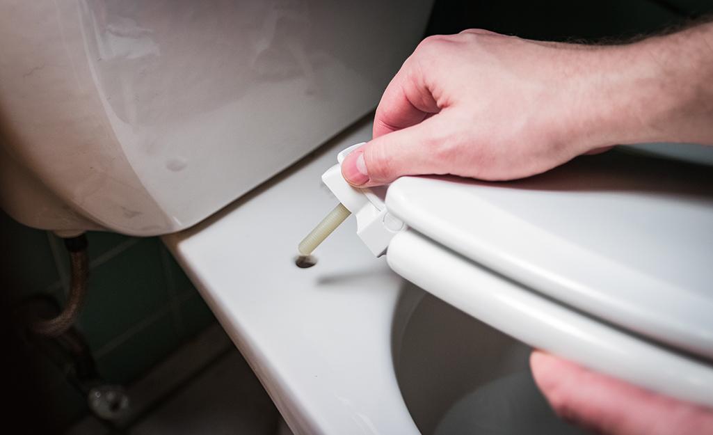 A person attaches a new toilet seat to a toilet bowl.
