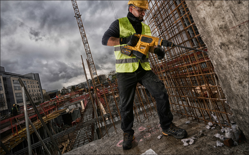 A construction worker using a hammer drill while wearing safety toe bits.