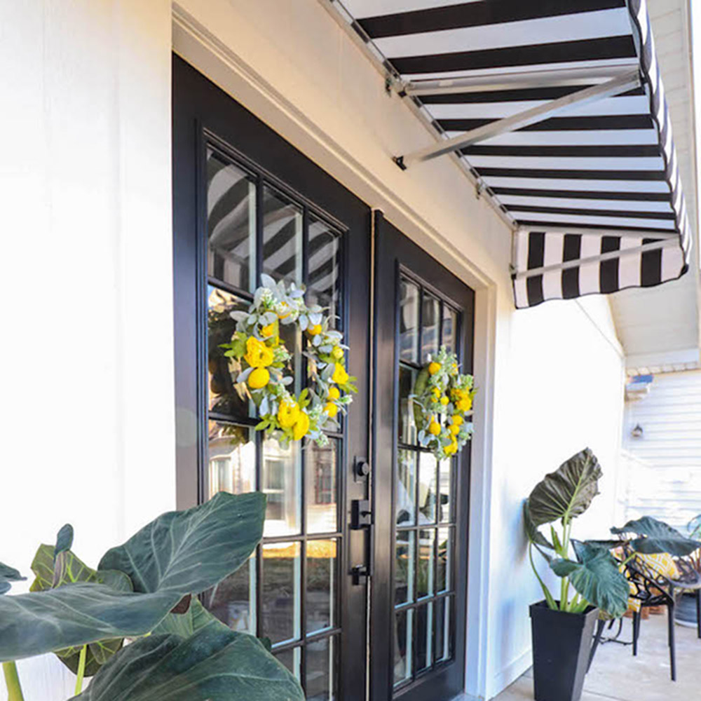 A black and white striped awning hangs over black double doors decorated with colorful wreaths.