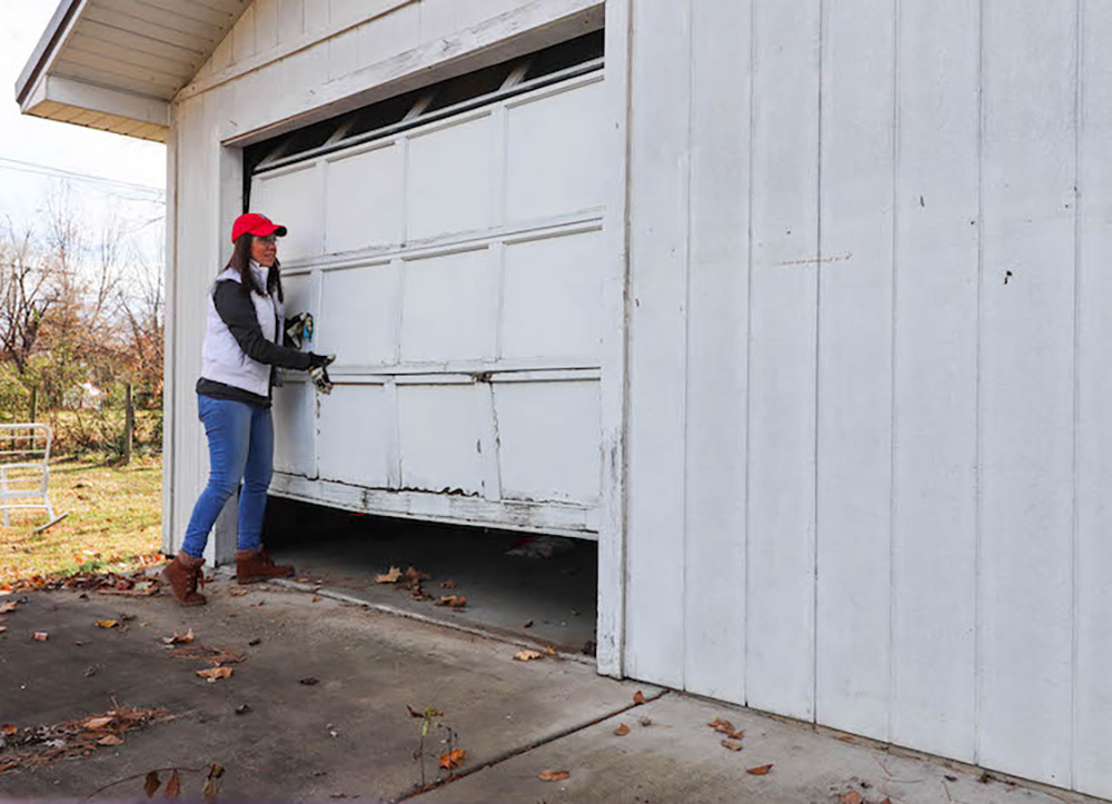 A woman lifting up an old garage door.