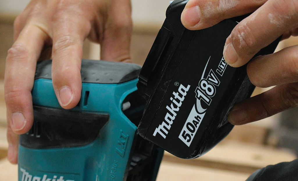 A person attaching a battery to an outdoor power tool.