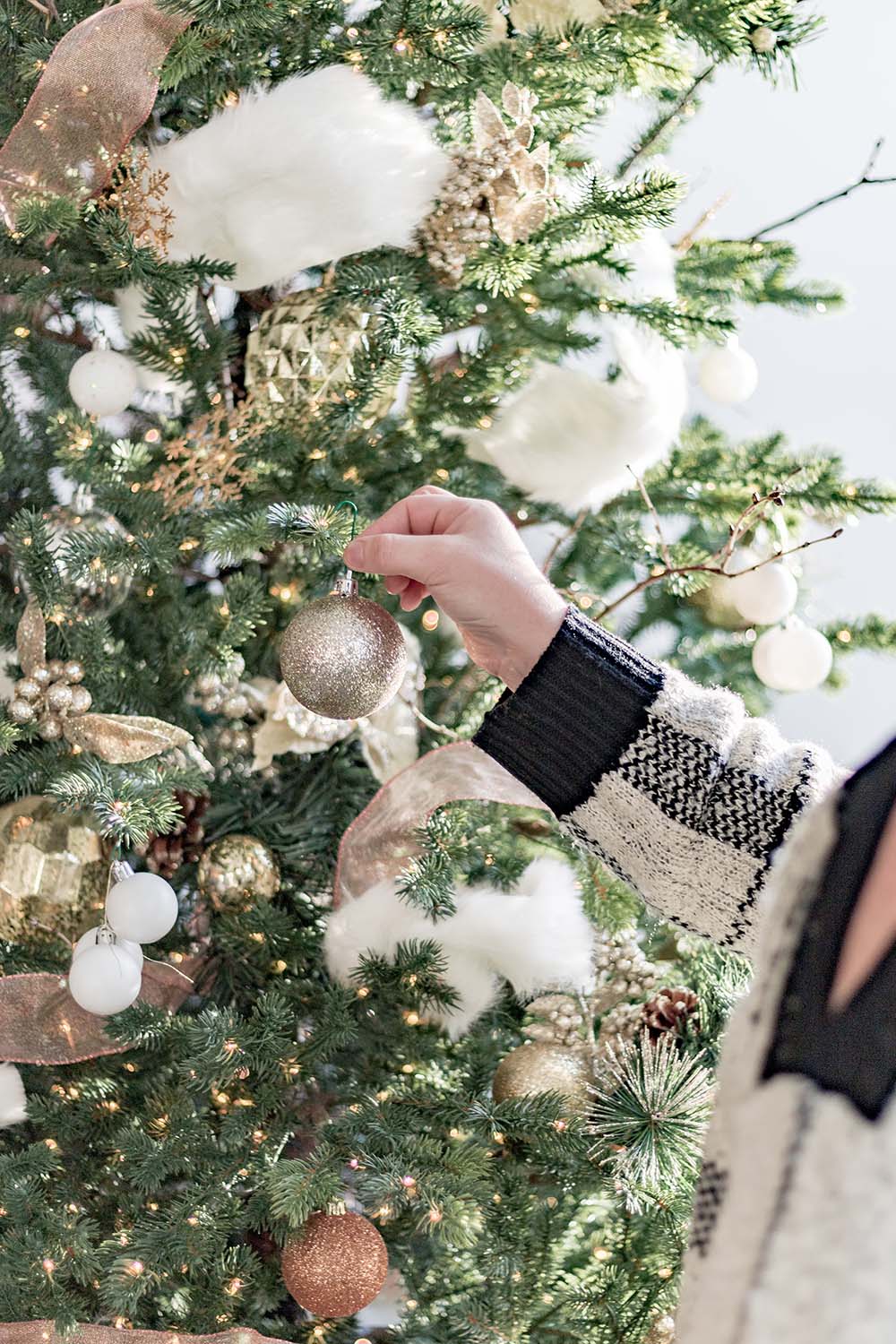 A woman adds a glitter ornament to a Christmas tree.