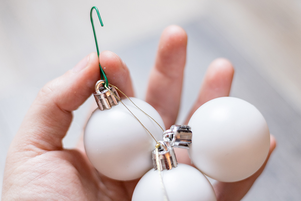 A person uses a hook and string to attach three small white ornaments together.