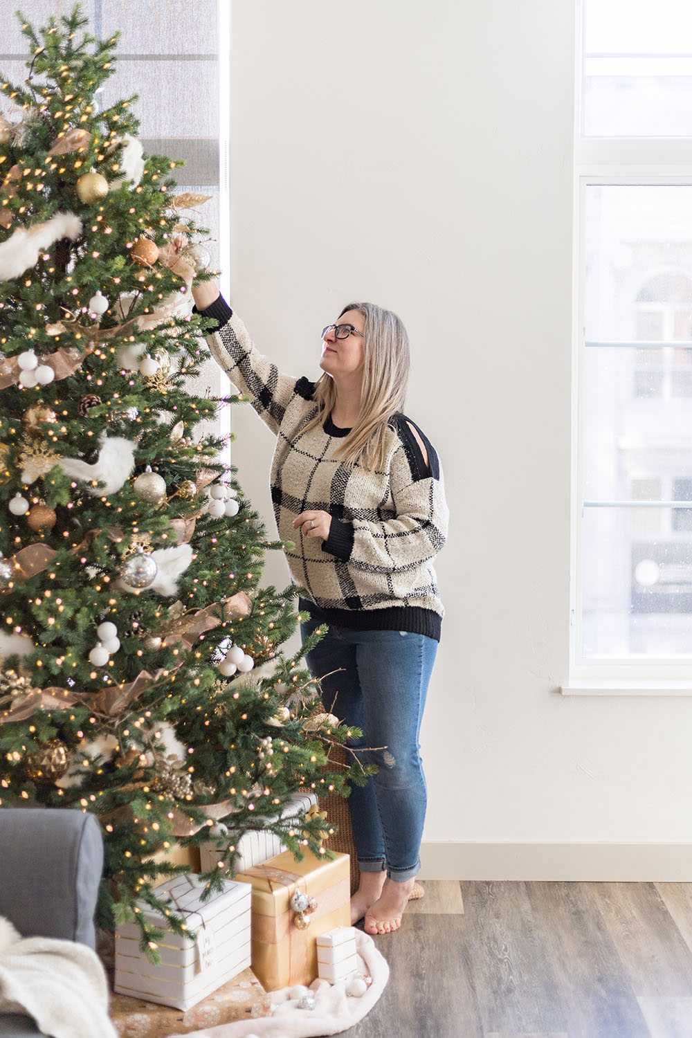 A woman stands on hardwood floors while decorating a Christmas tree.