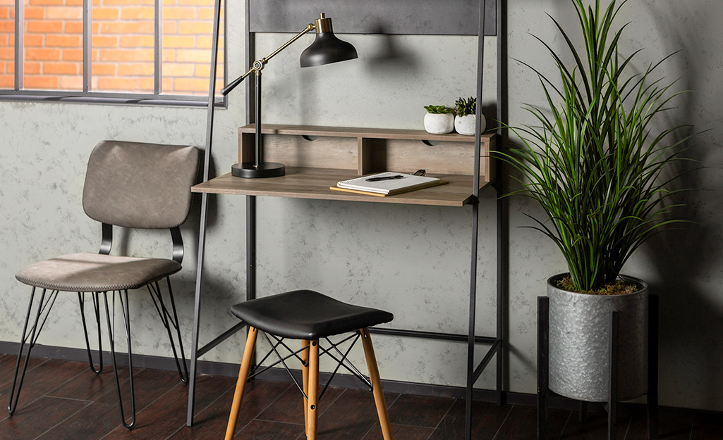 Industrial desk and backless stool sitting in front of gray wall.