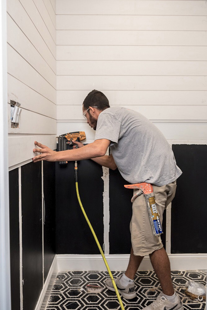 A man attaching shiplap in the corner of a room.