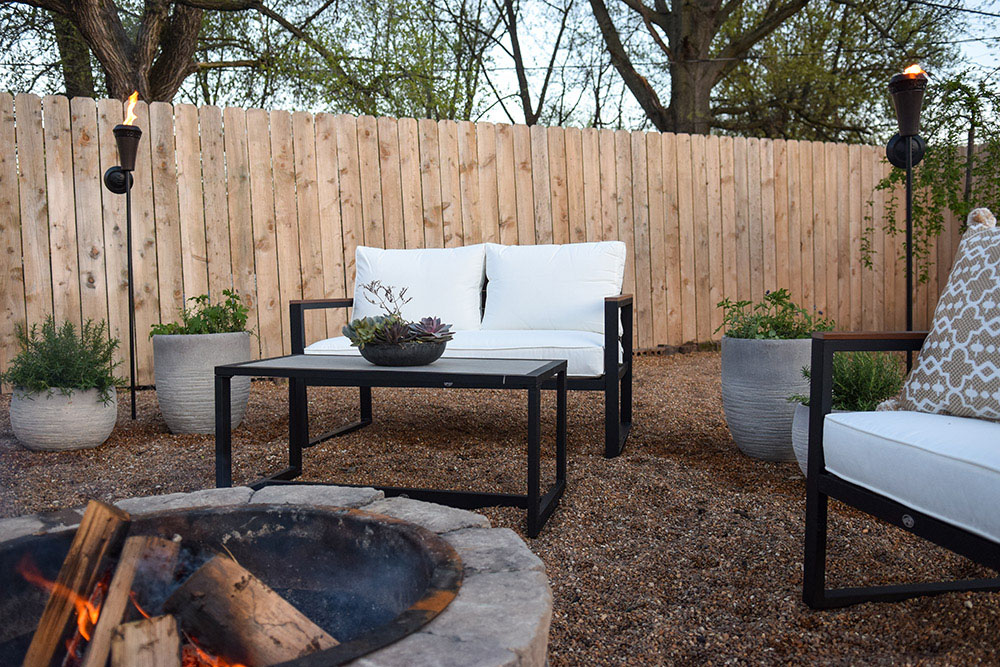 A fenced in backyard with modern outdoor furniture and a fire pit.