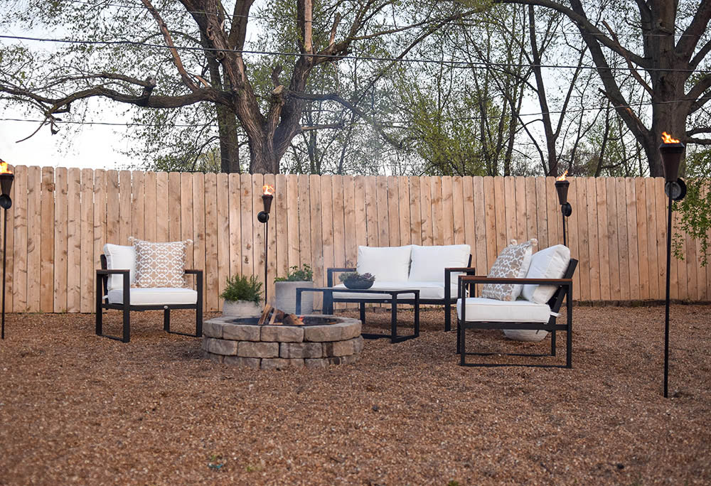A large backyard of gravel with a fire pit, modern outdoor seating, and tiki torches.