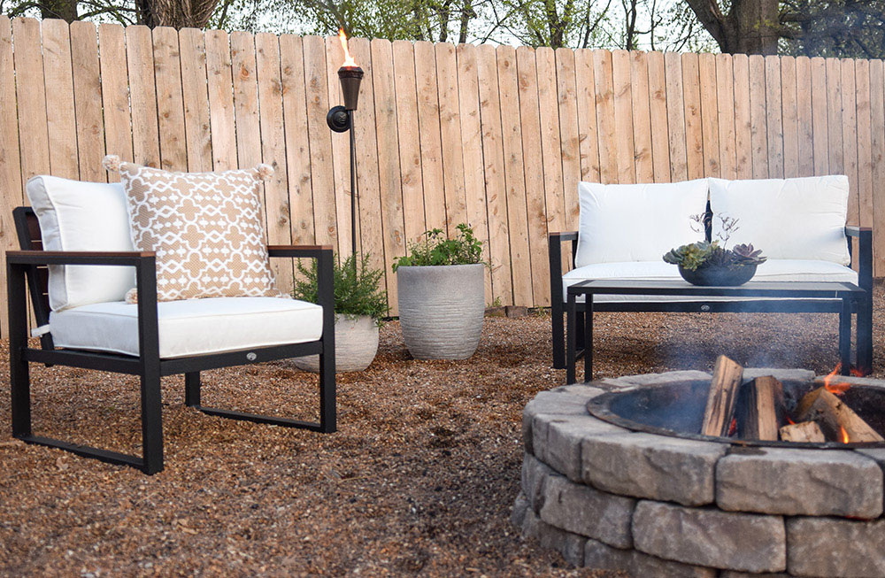 An outdoor chair in front of a fire pit is decorated with an outdoor pillow.