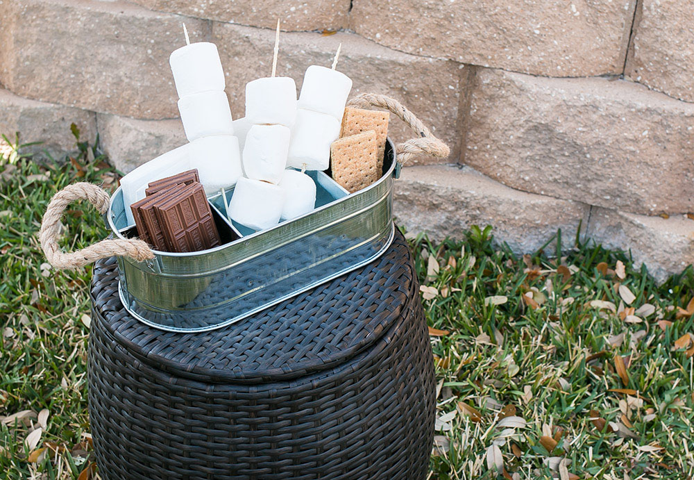 A metal tin filled with s'mores items sits on a wicker stool. A metal tin filled with s'mores items sits on a wicker stool.