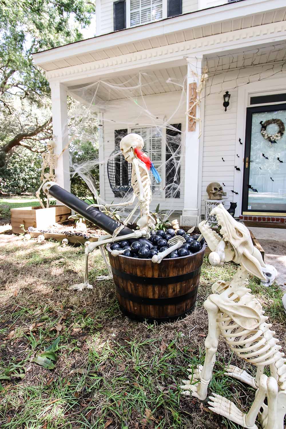 A pirate skeleton sitting in a barrel planter with a cannon and cannon balls.