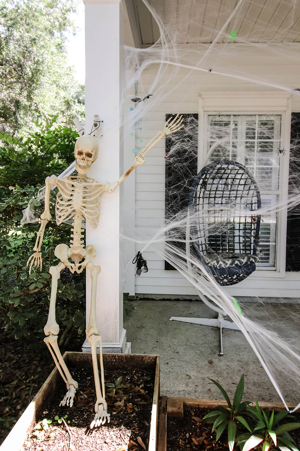 A skeleton standing in a garden bed next to a porch of spider webs.