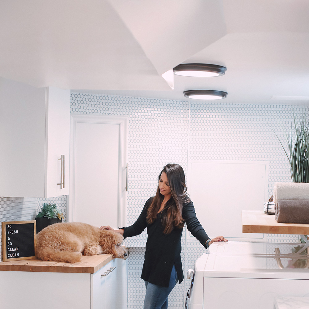 A woman petting a dog in a bright laundry room.