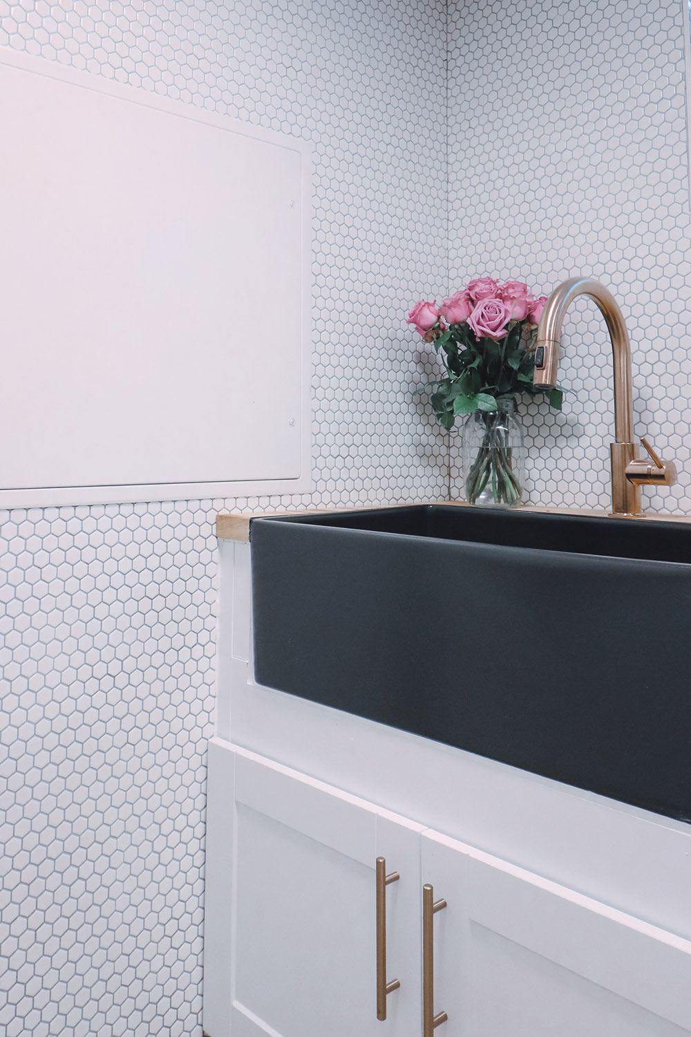 A black fireclay sink with a bronze faucet sits in a white shaker cabinet.