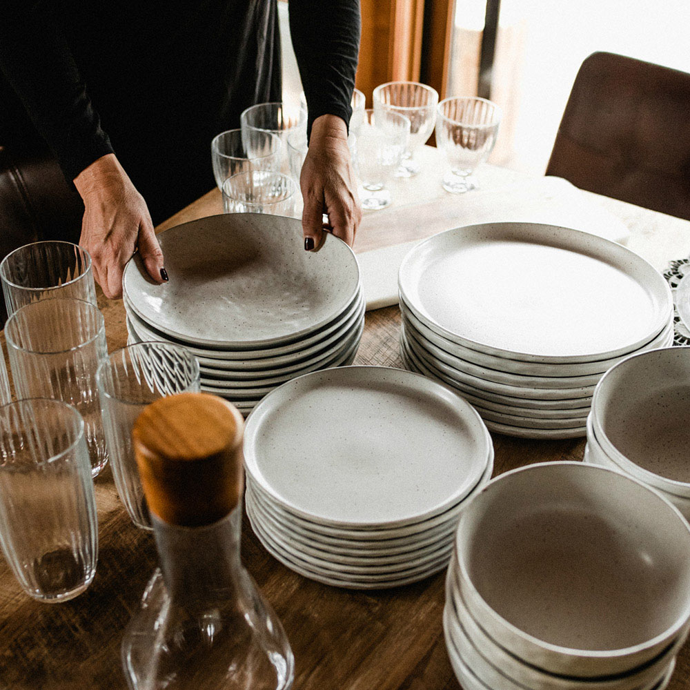 A person holding a plate on a table full of stacked plates.