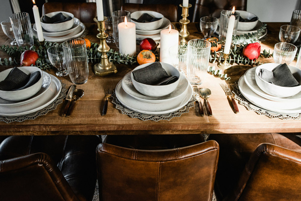 A wood table decorated with white dinnerware and black napkins.