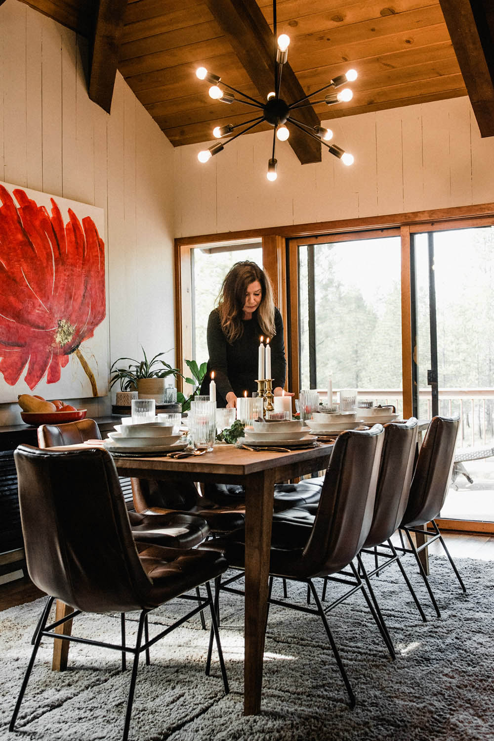 A woman standing behind a dining table below a chandelier.