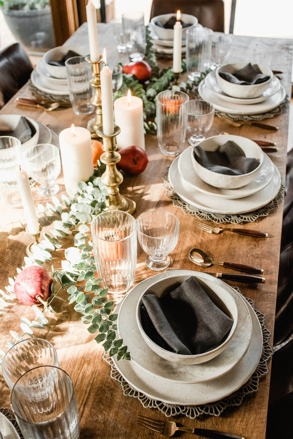 A wooden table with white place settings on decorative chargers.